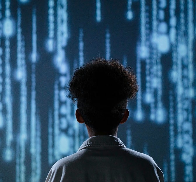 A person with curly hair faces a digital display of cascading blue binary code, immersed in a tech-inspired atmosphere.