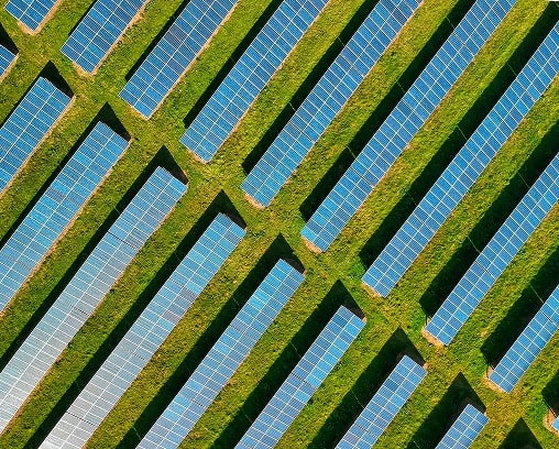 Aerial view of a solar farm, showcasing rows of solar panels alternating with lush green grass.